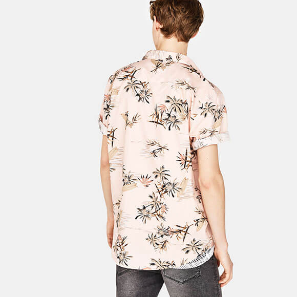 Back view of a man wearing a light pink tropical palm print shirt paired with dark gray jeans, styled for a relaxed fit. The shirt showcases premium quality fabric and design, ideal for men's fashion.