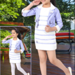 Little girl wearing a premium lilac faux leather jacket over a white and purple tiered fur dress, standing against a floral background.